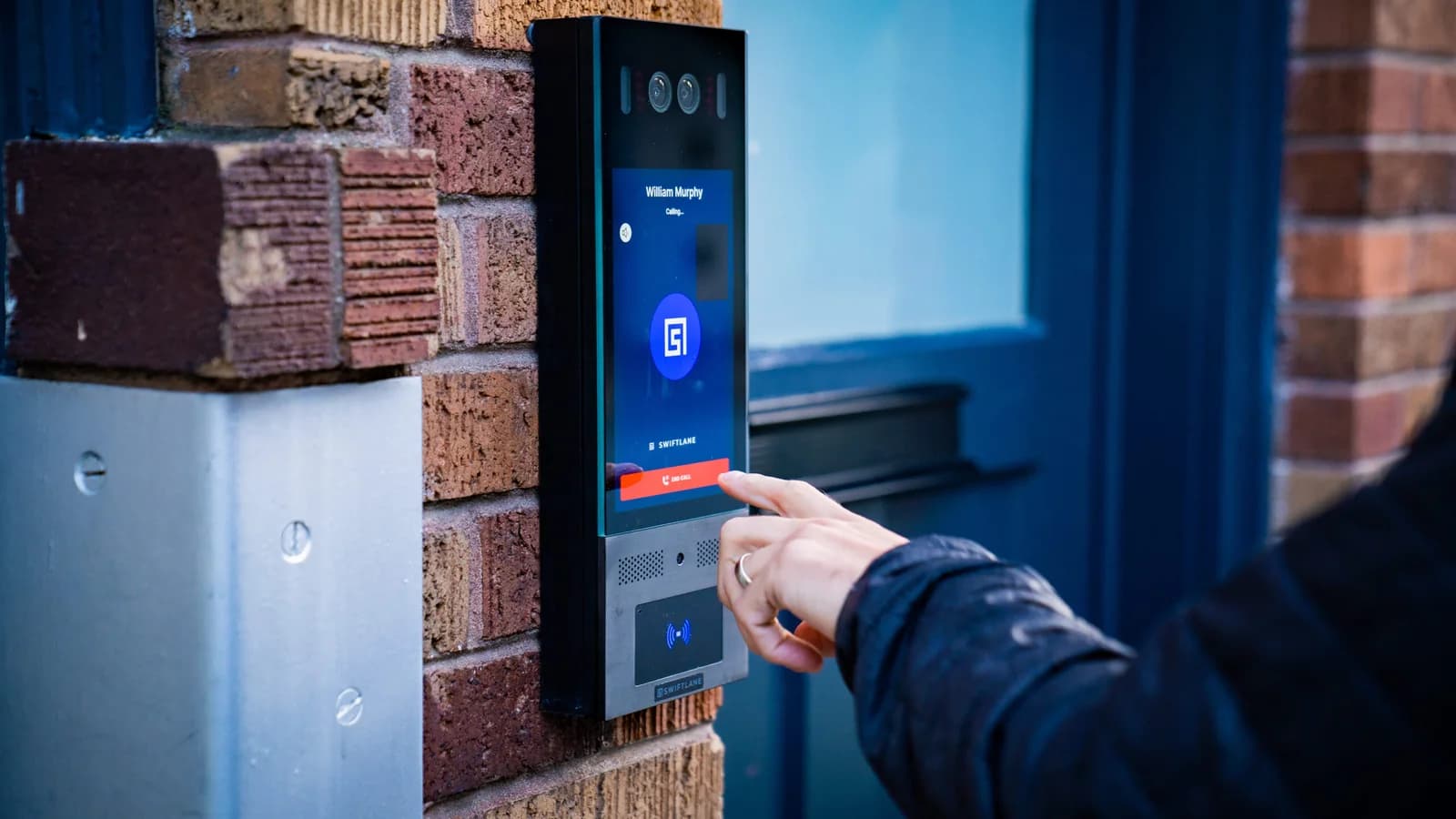 A visitor using a Swiftlane Swiftreader X video intercom beside an entrance.