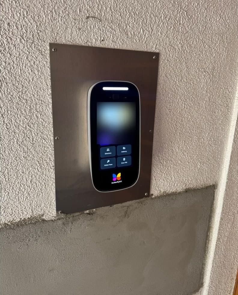 Before: a brass buzzer panel with speaker grilles and call buttons above a brass mailbox bank. After: a ButterflyMX touchscreen on a stainless steel plate on a stucco wall.