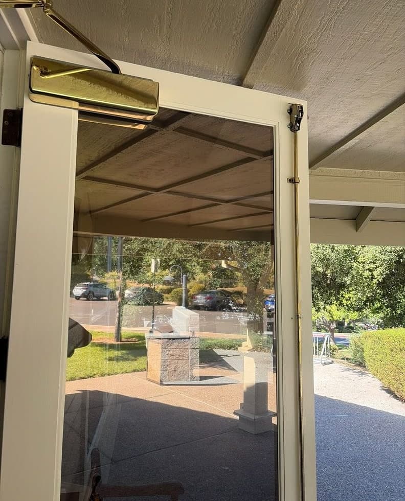 Before and after: the top of a white glazed door with no closer, then a brass surface closer and arm on the same door.