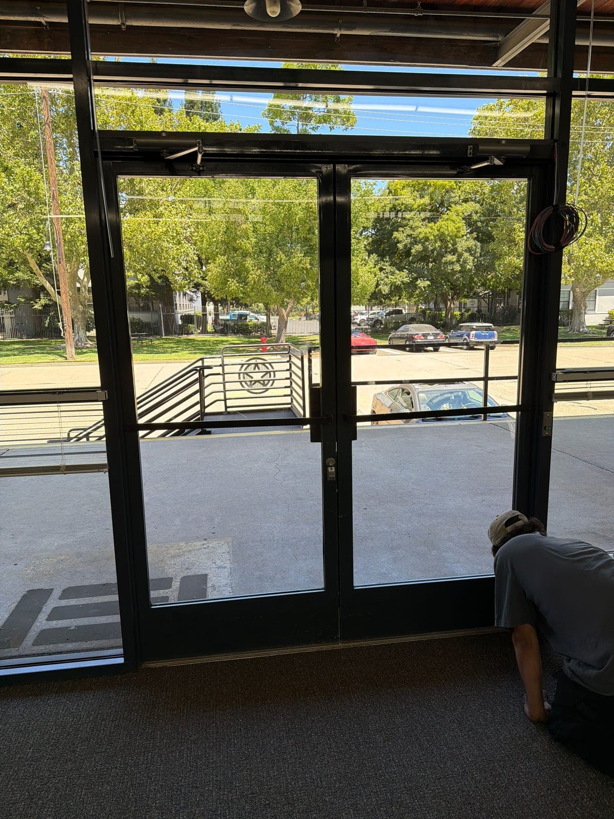 Technician kneeling at the base of a double glass entry door, with a coil of low-voltage wire hanging from the aluminum frame.