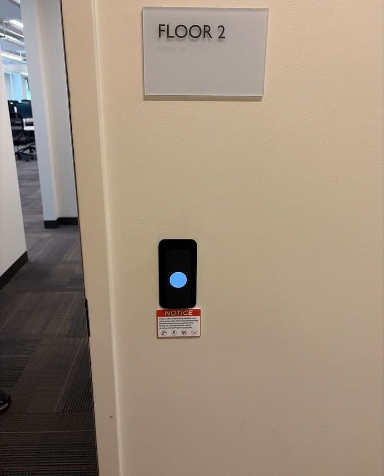 Before and after: a small black card reader with a red light below a Floor 2 sign, then a Kisi reader with a blue circle in the same spot below the same sign.