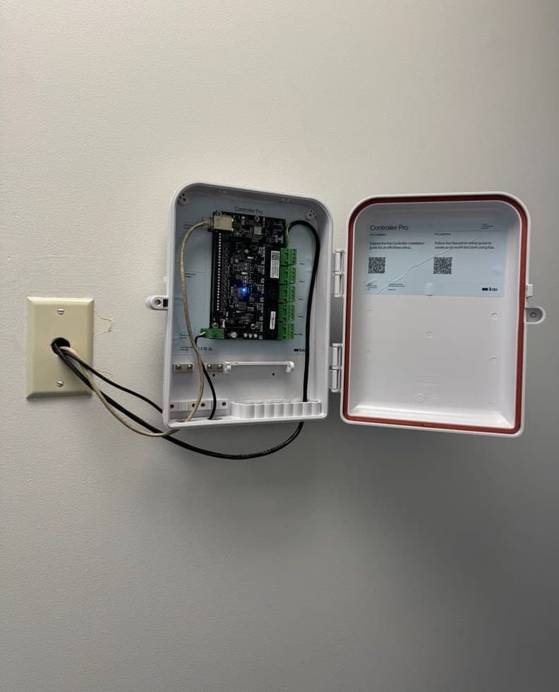 Before and after: a blank beige wall with a low-voltage wall plate and a loose cable, then a Kisi Controller Pro board inside an open white enclosure on the same wall, with cables entering from the wall plate.