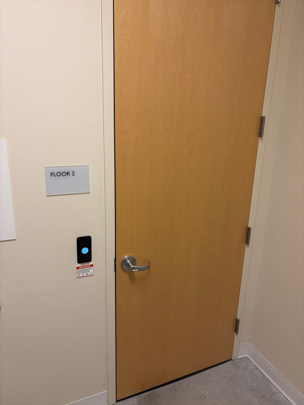 Wood office door with a Floor 2 sign and a black Kisi card reader mounted on the wall beside the latch side of the door.
