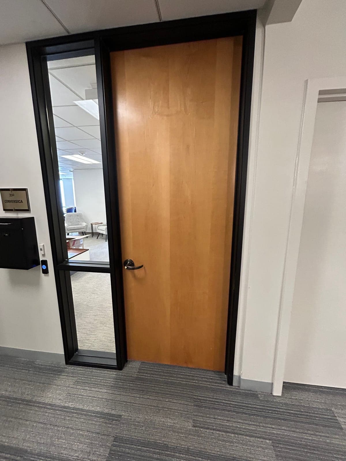 Office suite entry with a wood door, a tall glass sidelite, a suite sign and mailbox on the wall, and a small card reader beside the frame.