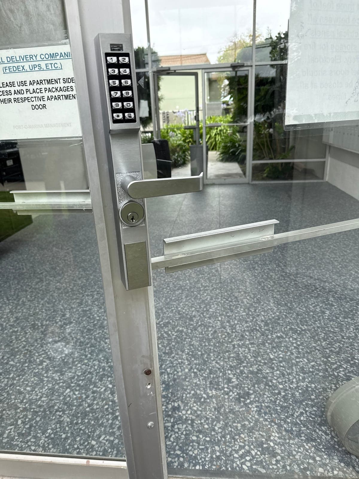 Close-up of a keypad trim with a lever handle and key cylinder mounted on the narrow aluminum stile of a glass door.