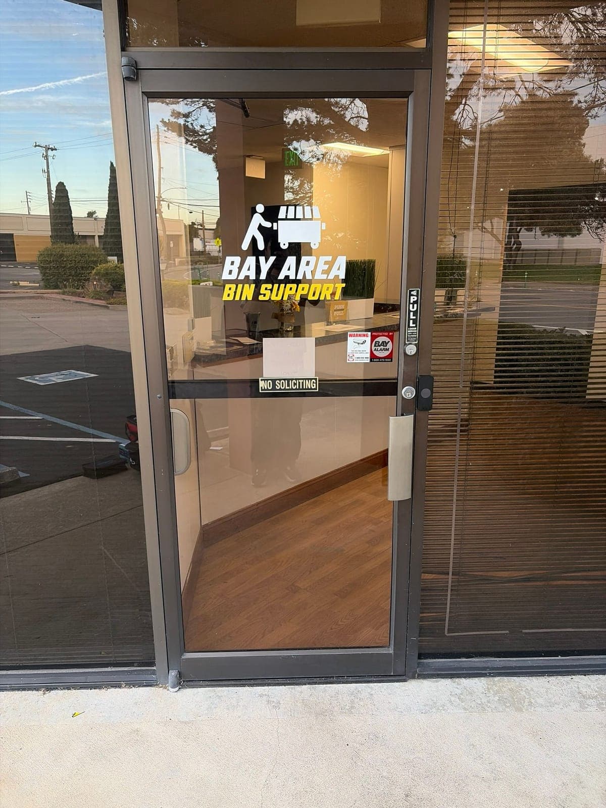 Dark aluminum storefront glass door with a business logo decal on the glass, a PULL sign, a pull handle and a small black Kisi reader on the frame.