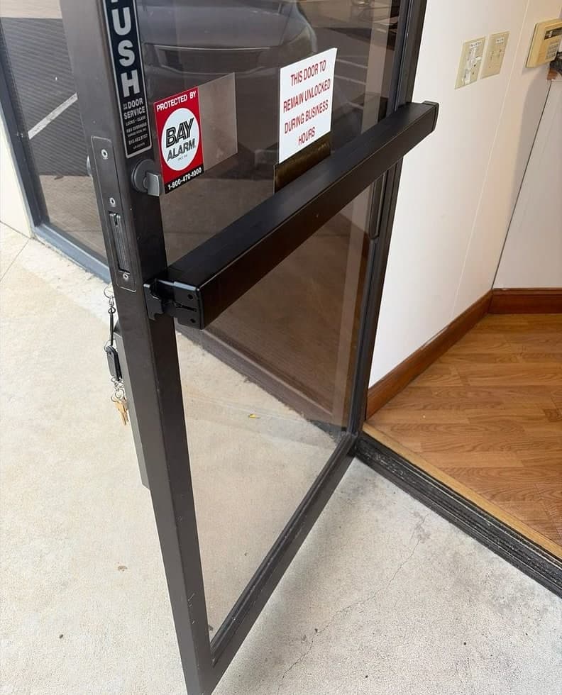 Before and after: a narrow-stile push pad on an aluminum glass door, then a full-width Adams Rite 8800 exit device on the same door.