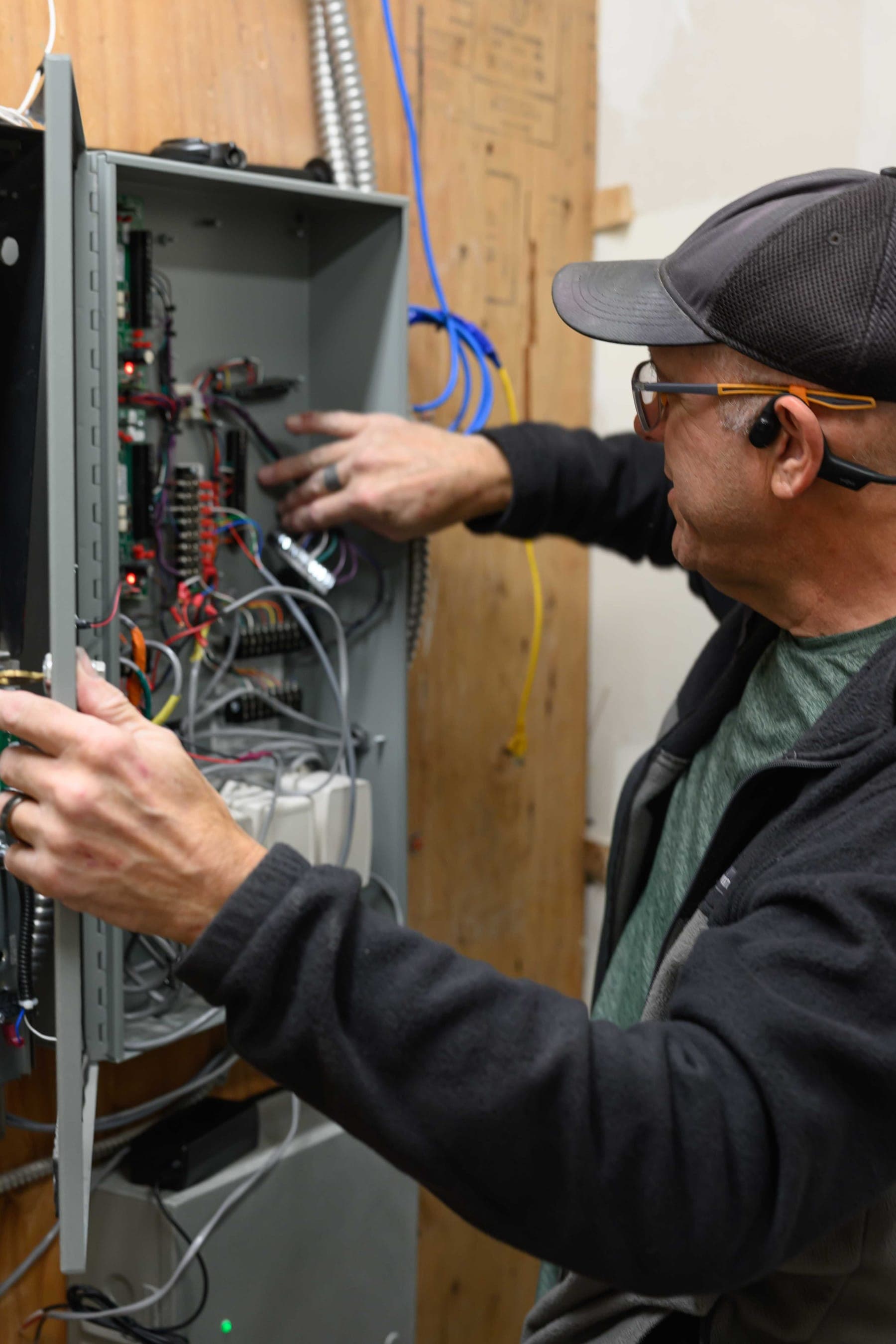 Elwin technician wiring the boards inside an open access-control cabinet mounted on a plywood backboard, with conduit and cable runs above.
