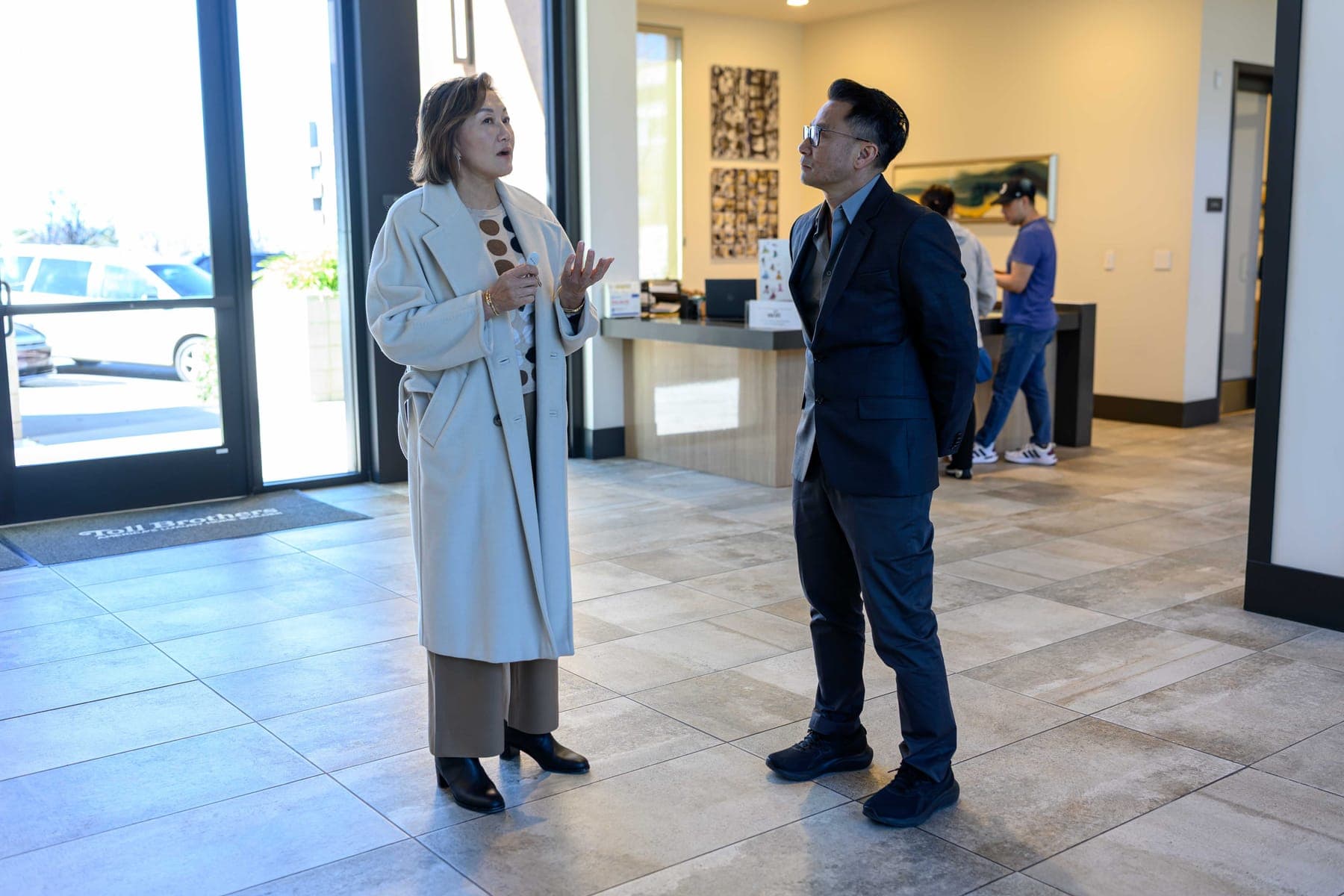 An Elwin consultant talking with a client in a bright lobby, with a reception desk and glass entry doors behind them.