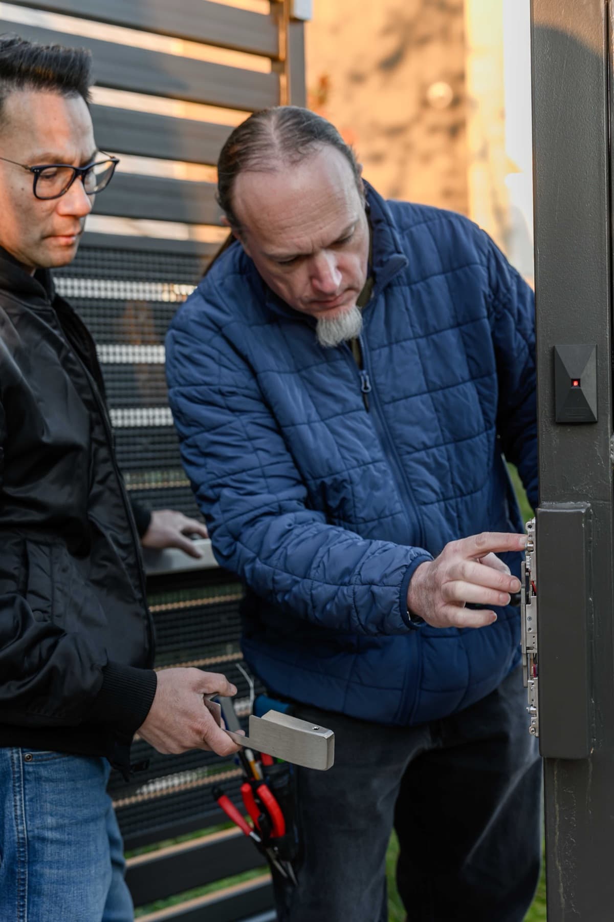 Two Elwin technicians inspecting electrified release hardware on a Bay Area gate post at dusk.