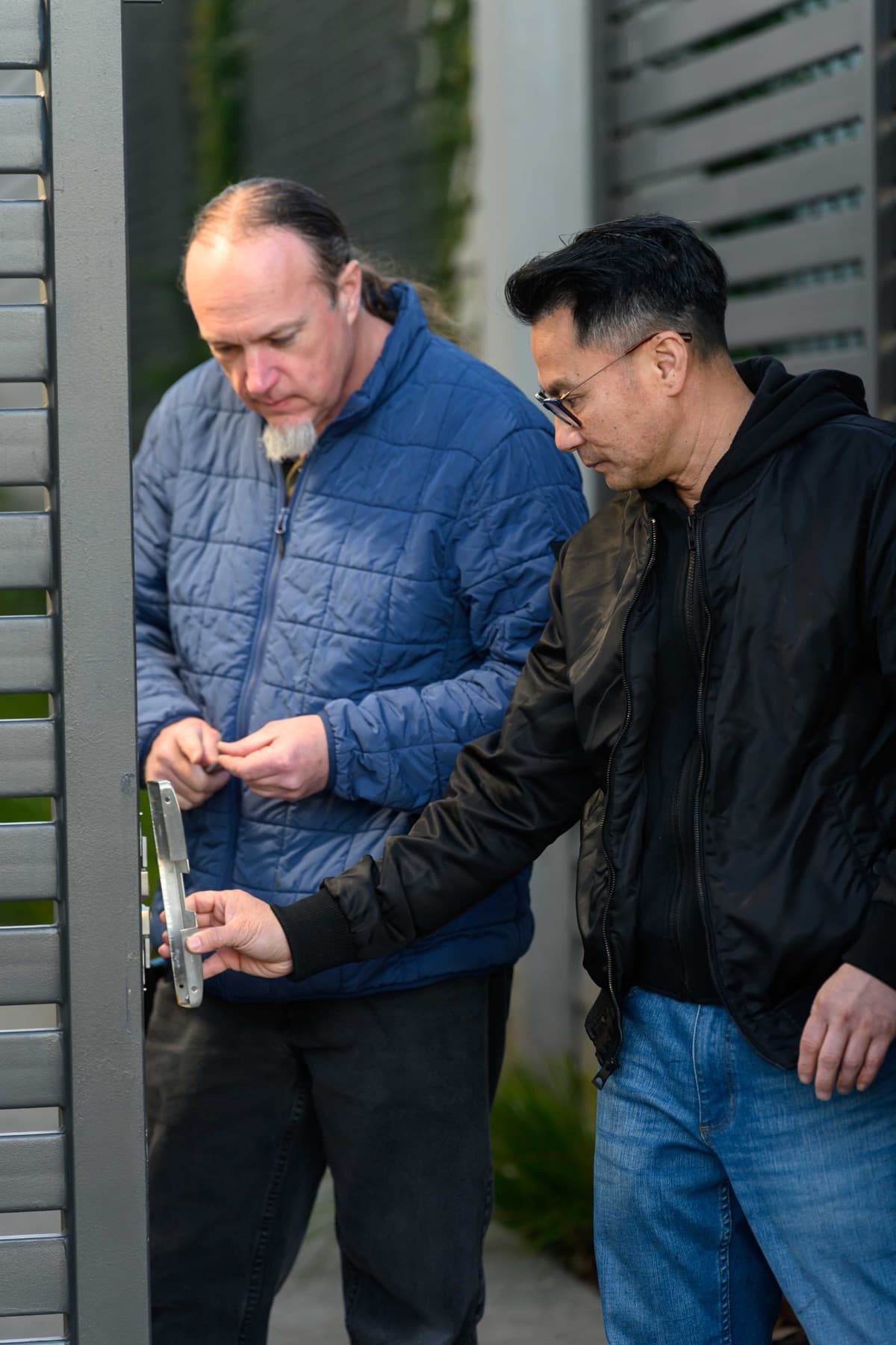 Elwin technician holding a strike plate against a gate frame while a colleague prepares fasteners.